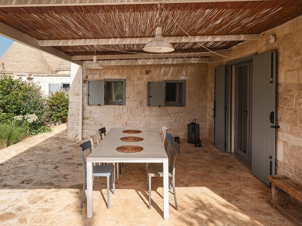 An outdoor dining area with a table and chairs, a pergola overhead, and stone walls. - Trulli near Fontanella, with a pool (Martina Franca)