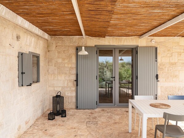 A covered patio with a stone wall, a table and chairs, a sliding glass door, and a hanging light fixture.