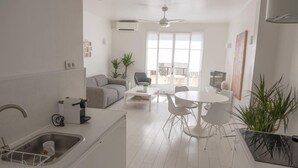 Een moderne keuken met witte apparaten, een eethoek met een ronde tafel en stoelen, en een balkon met uitzicht.