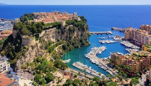 A coastal cityscape with a historic fort, a marina with numerous boats, and residential buildings.