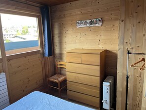 Ein Zimmer aus Holz mit einem Bett, einem Schminktisch, einem Stuhl und einer Heizung.