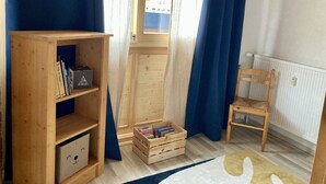A room with a wooden bookshelf, a small wooden chair, a window with curtains, and a radiator.