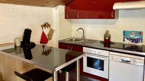 A compact kitchen with a wooden ceiling, red cabinets, a stainless steel sink, and a white dishwasher.