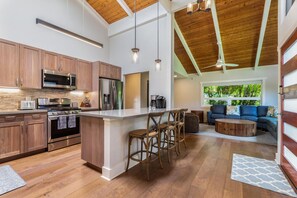A modern kitchen with wooden cabinets, stainless steel appliances, and a central island with bar stools. - Lani Oasis: Tropical North Shore Retreat w/ Pool, Hot Tub & AC (Princeville)