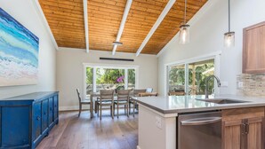 Une cuisine moderne avec un plafond en bois, un grand îlot central doté d’un évier et un coin repas avec des chaises et une table.