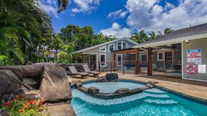 Un espace piscine avec des chaises longues, un jacuzzi et une maison sur laquelle est apposé un panneau d’avertissement.
