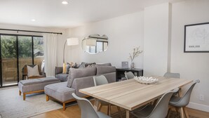 A modern living room with a wooden dining table, grey upholstered sofas, and a large mirror. - Steps from Riverfront Gondola, Modern Cozy Condo, Free Underground Parking (Avon)