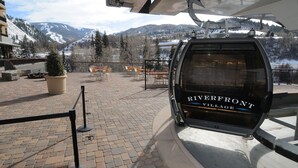 A ski lift with 'Riverfront Village' signage, a paved area with a potted tree, and a view of snow-covered mountains. - Steps from Riverfront Gondola, Modern Cozy Condo, Free Underground Parking (Avon)