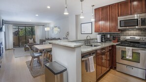 A modern kitchen with a dishwasher, oven, and microwave. There is a dining area with a table and chairs. - Steps from Riverfront Gondola, Modern Cozy Condo, Free Underground Parking (Avon)