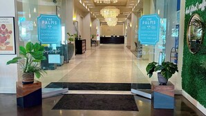 Een hotel lobby met een kroonluchter, glazen deuren en borden voor 'The Palms Coffeehouse', 'Sports Lounge' en 'Good Vibes Bar'.