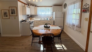A kitchen with white cabinets, a wooden dining table, and a window with sheer curtains. - Lakefront Tranquility/Fishermans Delight (New Hartford)