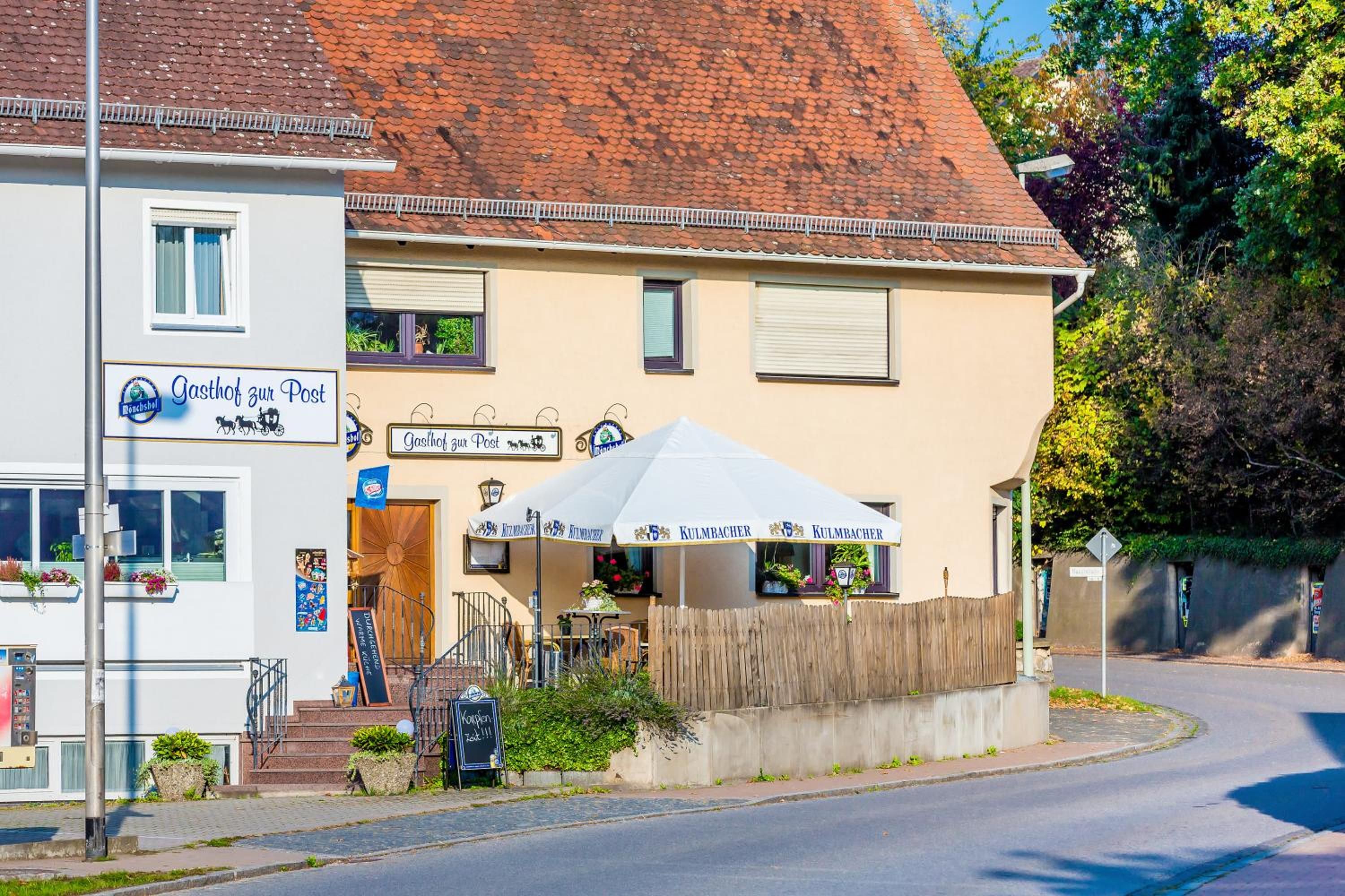 Un bâtiment portant une enseigne indiquant « Gasthof zur Post » et disposant d’un espace extérieur couvert avec des parasols.