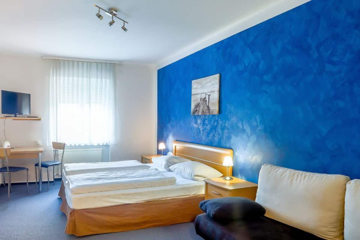 Une chambre d’hôtel avec un grand lit, un bureau avec une chaise, une télévision et un mur d’accent bleu.