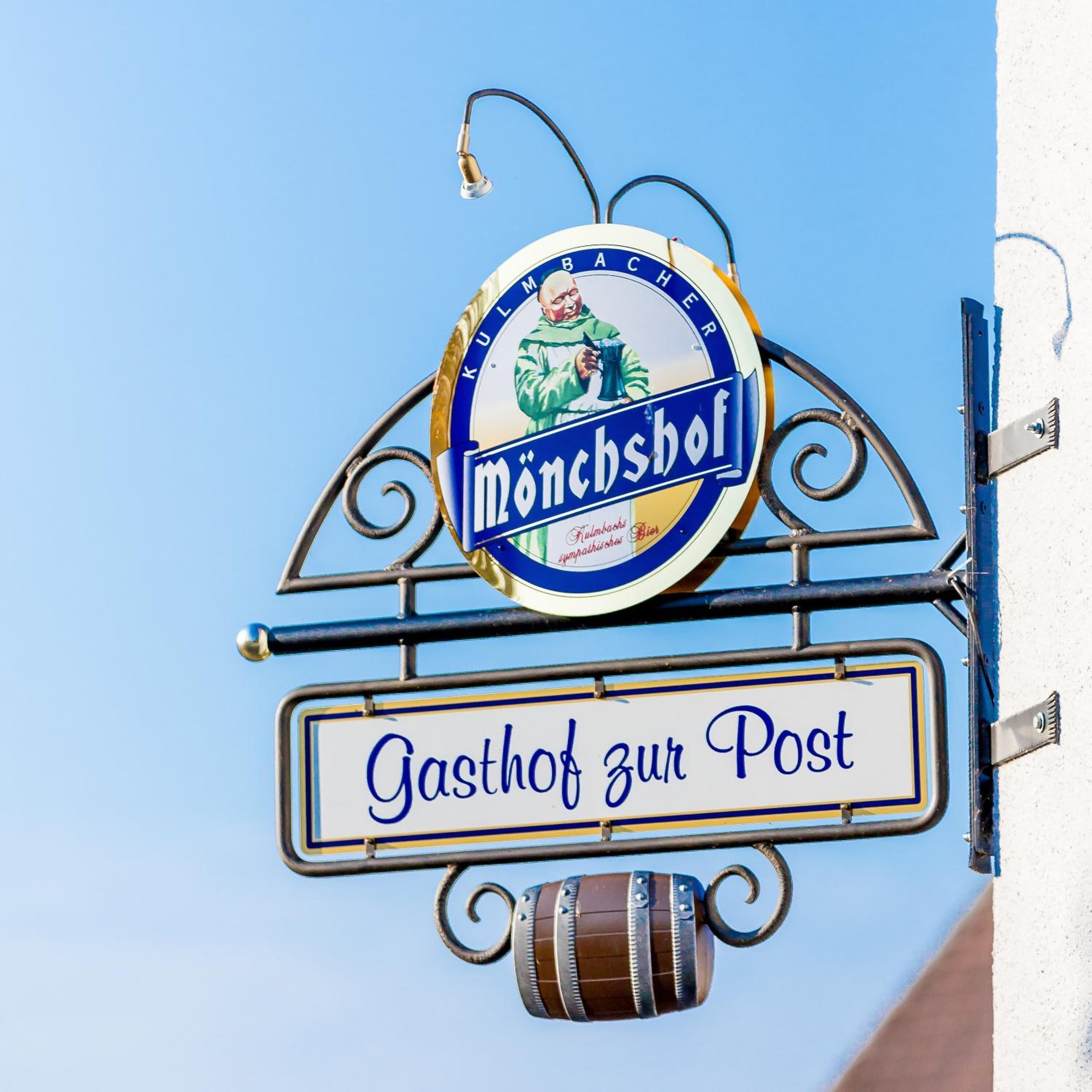 A beer sign with the name "Mönchshof" and a street sign below it reading "Gasthof zur Post".