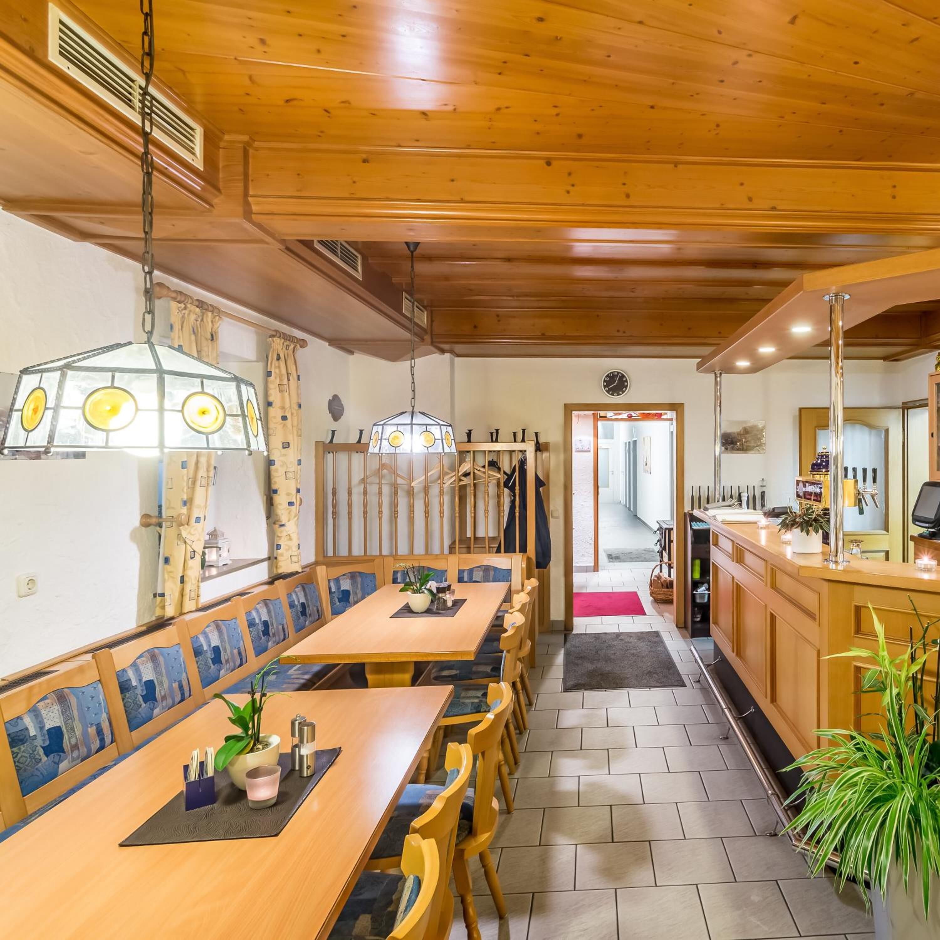 Un restaurante con mesas y sillas de madera, una zona de bar y vistas a la calle.