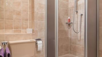 A bathroom with beige tiles, a toilet, a shower with a handheld showerhead, and a towel rack with purple towels.
