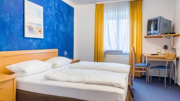 Habitación de hotel con cama doble, escritorio con silla, televisor en un estante y un cuadro en la pared.