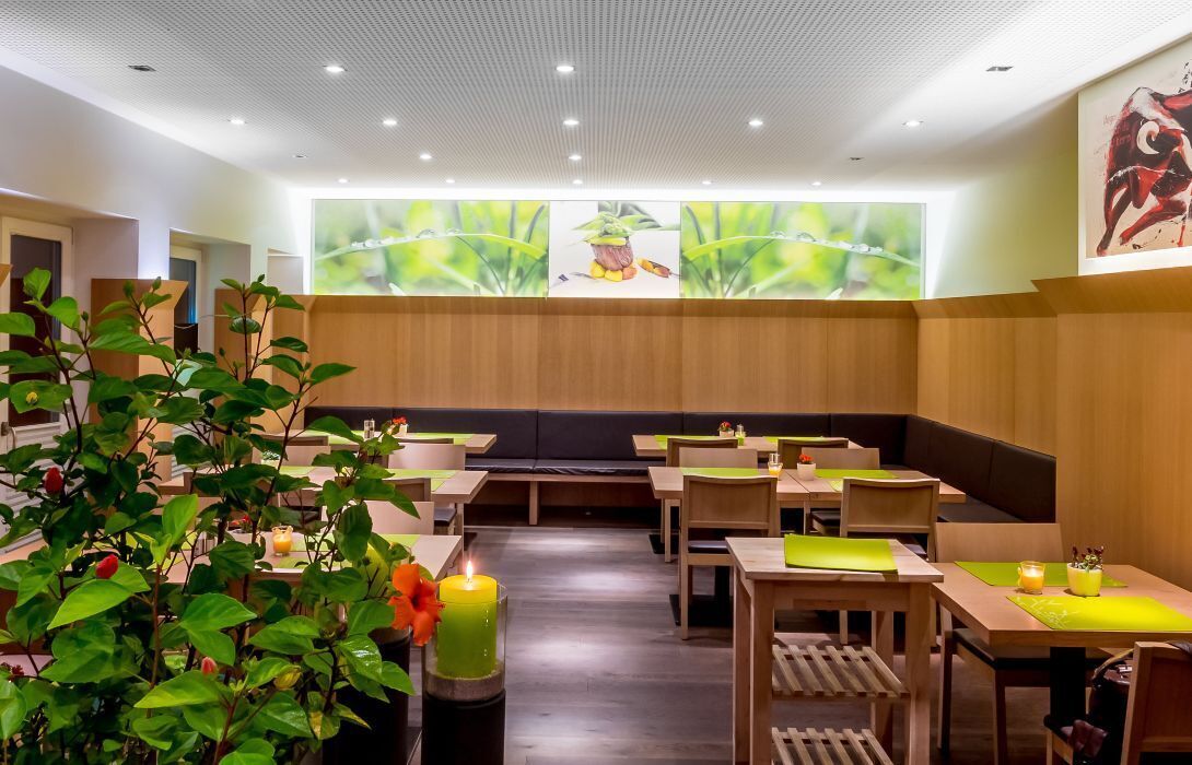 Un restaurante con mesas y bancos de madera, plantas verdes y un mural de temática natural.