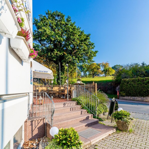 A restaurant with outdoor seating, a staircase leading to the entrance, and a hedge in the foreground. - Gasthof Alte Post (Aurachtal)