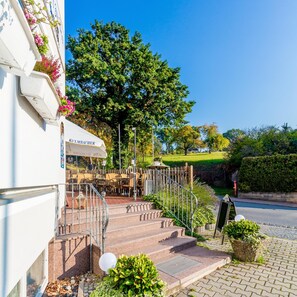 Un restaurant doté d’une terrasse, d’un escalier menant à l’entrée et d’une haie au premier plan.