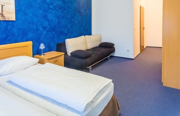 Une chambre d’hôtel avec un lit, une table de chevet, un canapé et un mur bleu à texture.