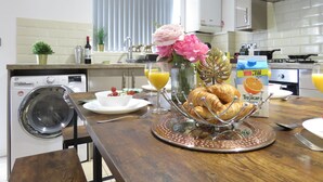 Een keuken met een houten tafel gedekt voor het ontbijt, met croissants, sinaasappelsap en een vaas met bloemen.