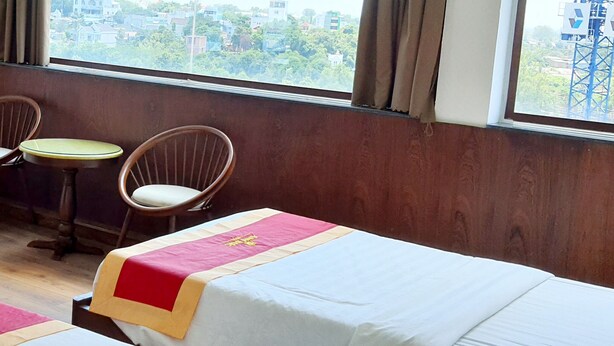 A hotel room with a bed, a desk, two chairs, and a window with a view of buildings. - HANZ Anh Duc Hotel Binh Duong (Ho Chi Minh City)