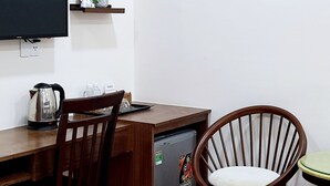 A compact room with a wooden desk, a chair, a television mounted on the wall, and a small refrigerator. - HANZ Anh Duc Hotel Binh Duong (Ho Chi Minh City)