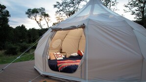 A dome-shaped tent with a bed inside, a doormat with 'hello' written on it, and a wooden deck.