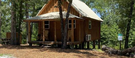 A wooden cabin with a porch, surrounded by trees.
