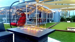 Ein Terrassenbereich im Freien mit Feuerstelle, Sitzgelegenheiten und einem überdachten Sitzbereich mit Lichterketten.