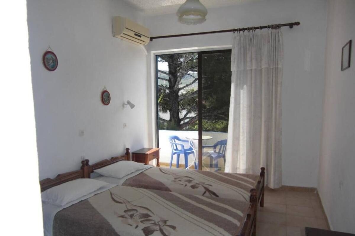 A bedroom with a bed, a small table, and a window with a view of outdoor furniture.