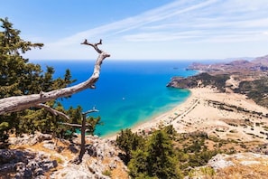 A coastal landscape with a clear view of the sea, a beach, and a mountainous backdrop. - Anthoula Sun (Rhodes)