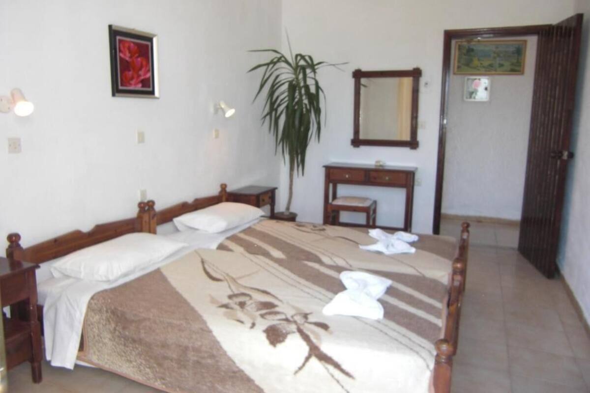 A bedroom with a bed, bedside tables, a mirror, a dresser, and a potted plant.