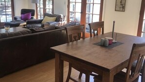 A dining area with a wooden table and chairs, a sofa with cushions, and a view through large windows. - Topanga Deck House light spacious, amazing mountain views, huge deck under Oaks (Topanga)