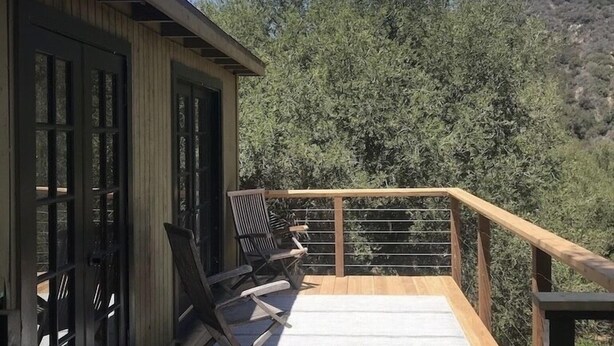 A wooden deck with a railing, two chairs, and a view of trees and hills. - Topanga Deck House light spacious, amazing mountain views, huge deck under Oaks (Topanga)