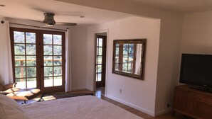 A bedroom with a large bed, a ceiling fan, a TV on a wooden cabinet, and a view of the outdoors through a door and window. - Topanga Deck House light spacious, amazing mountain views, huge deck under Oaks (Topanga)