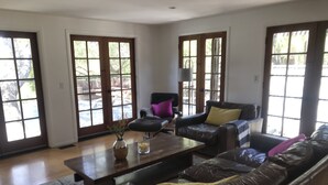 A spacious living room with a leather sofa, a coffee table, and a chair. There are large windows with a view of the outdoors. - Topanga Deck House light spacious, amazing mountain views, huge deck under Oaks (Topanga)
