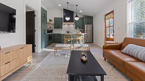 Una cocina moderna con armarios verdes, un comedor con dos sillas, una mesa negra y un sofá de cuero marrón.