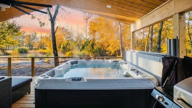 Un jacuzzi bajo una terraza de madera, con vistas a árboles otoñales.