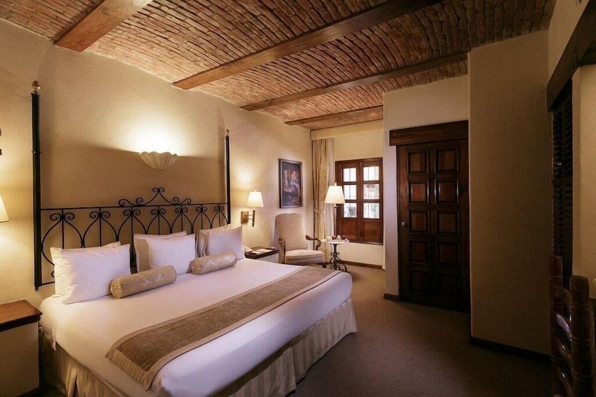 A hotel room with a large bed, two bedside tables, a wooden ceiling, and a door with a window.