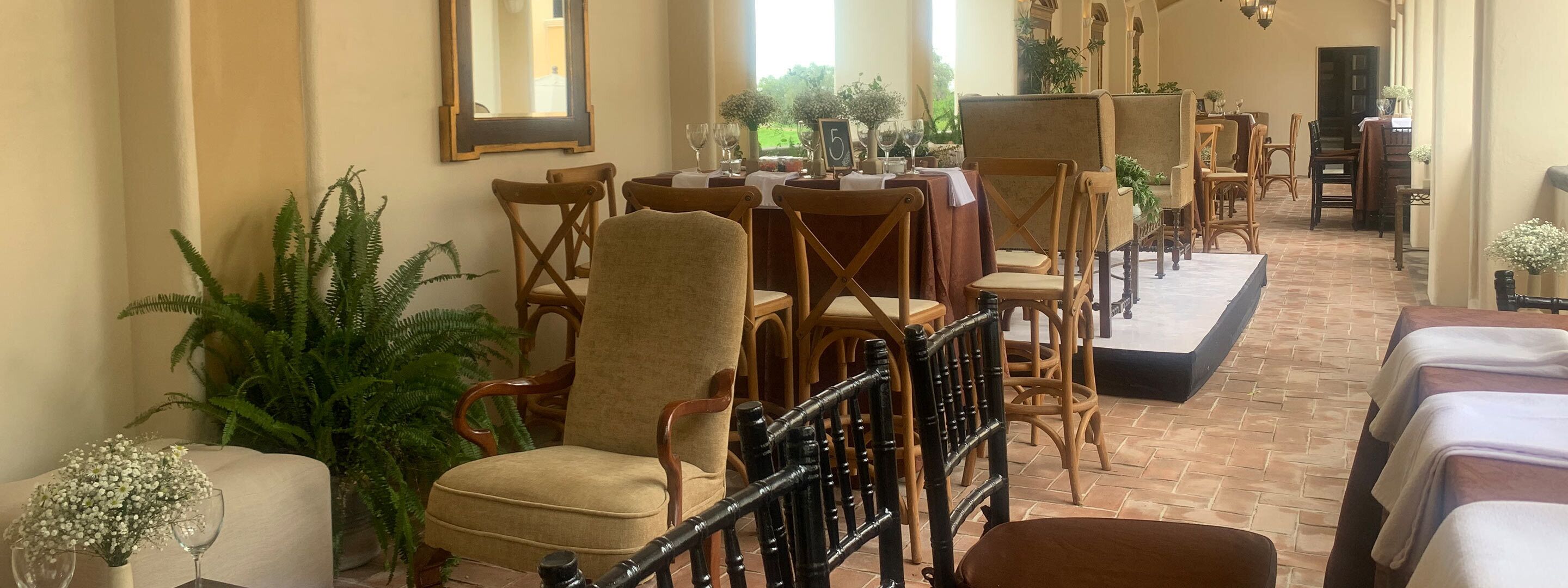 Un comedor de hotel con sillas y mesas de madera, plantas en macetas y suelo de ladrillo.