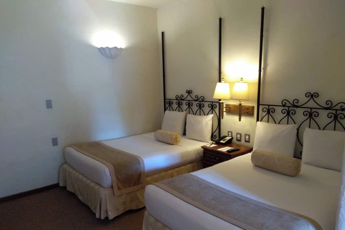 Una habitación de hotel con dos camas individuales, cada una con una mesita de noche, una lámpara y un teléfono.