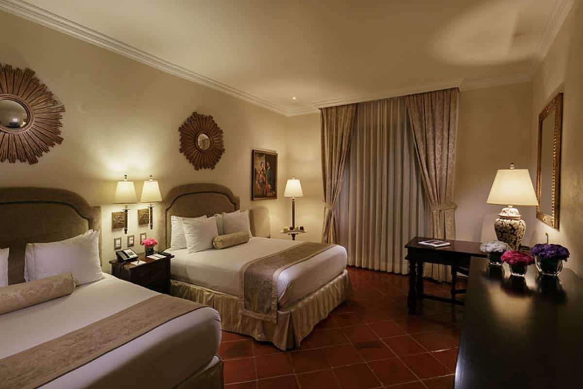 Habitación de hotel con dos camas, un escritorio, una lámpara y un espejo.