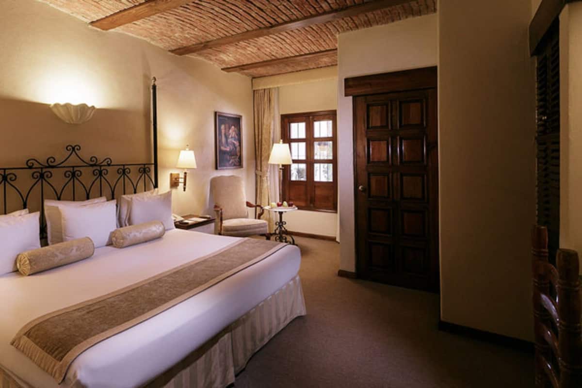 Una cama grande con cabecera, dos lámparas de noche, mesitas y una puerta de madera.