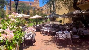 An outdoor dining area with tables and chairs, umbrellas, and a building with a dome in the background. - Villa Antigua (Tequisquiapan)