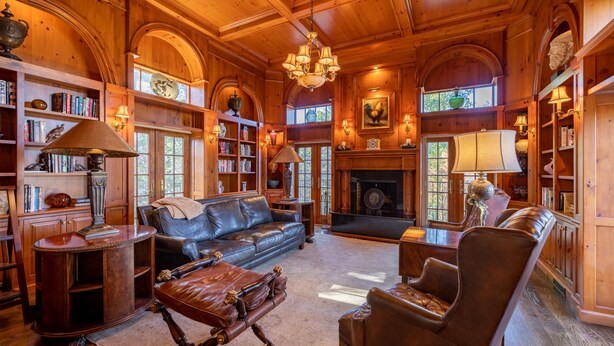 A cozy, wooden-furnished living room with a fireplace, leather furniture, and a bookshelf.