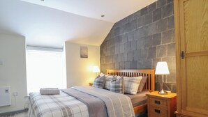 Une chambre à coucher avec un lit, deux tables de chevet, une armoire en bois et un mur en pierre.