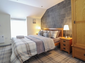 A bedroom with a bed, two bedside tables, a wooden wardrobe, and a stone wall.