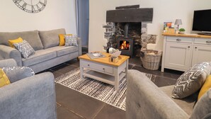 Un salon avec un canapé gris, une table basse, une cheminée, un téléviseur et une horloge au mur.